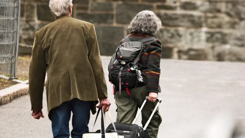 Pareja mayor caminando con sus maletas por una calle empedrada
